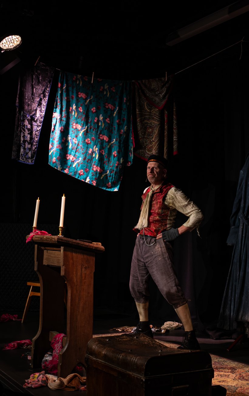 Steve Furst as Fagin, hands on hips atop a travelling trunk
