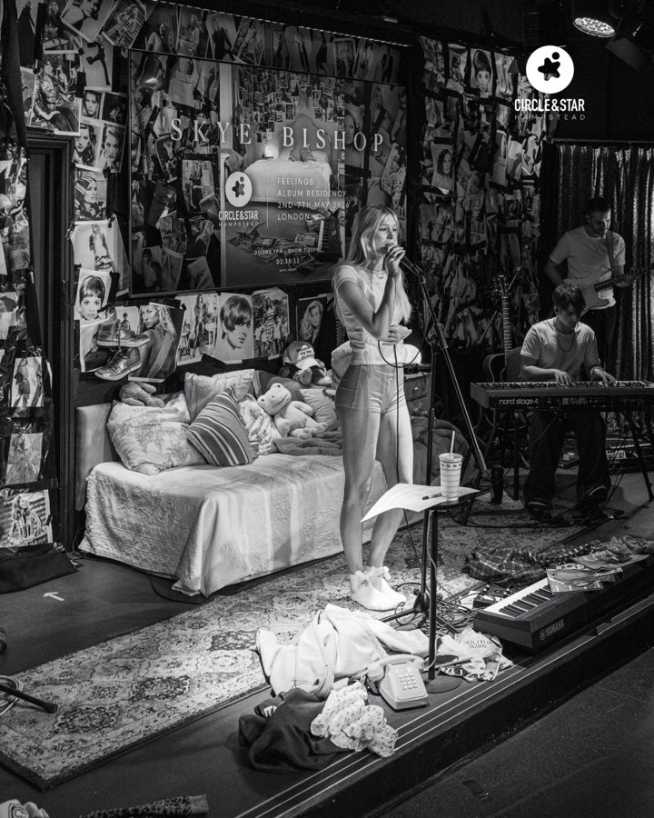The stage dressed as a bedroom, walls papered with photographs, a band playing